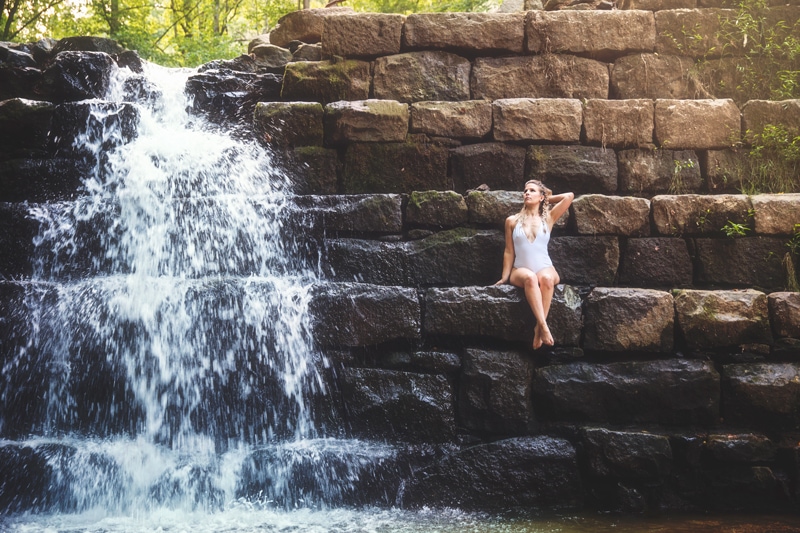 Portrait Photographer, woman sitting on giant stones next to waterfall