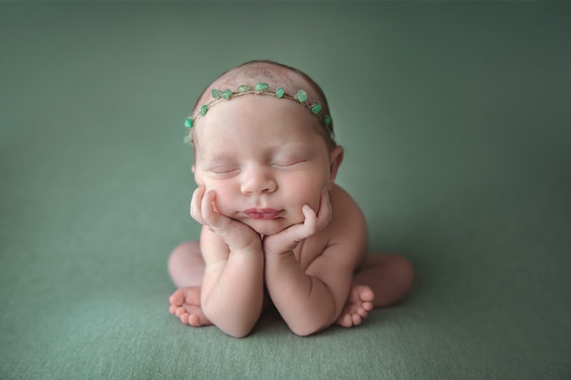 Newborn Photography, baby with greenery headband sitting with head in its hands